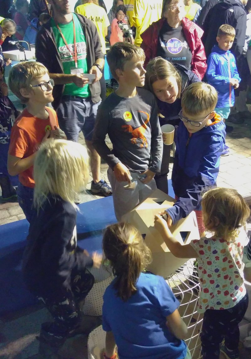 Six children playing with the wood virus interface, with some adults in the background.